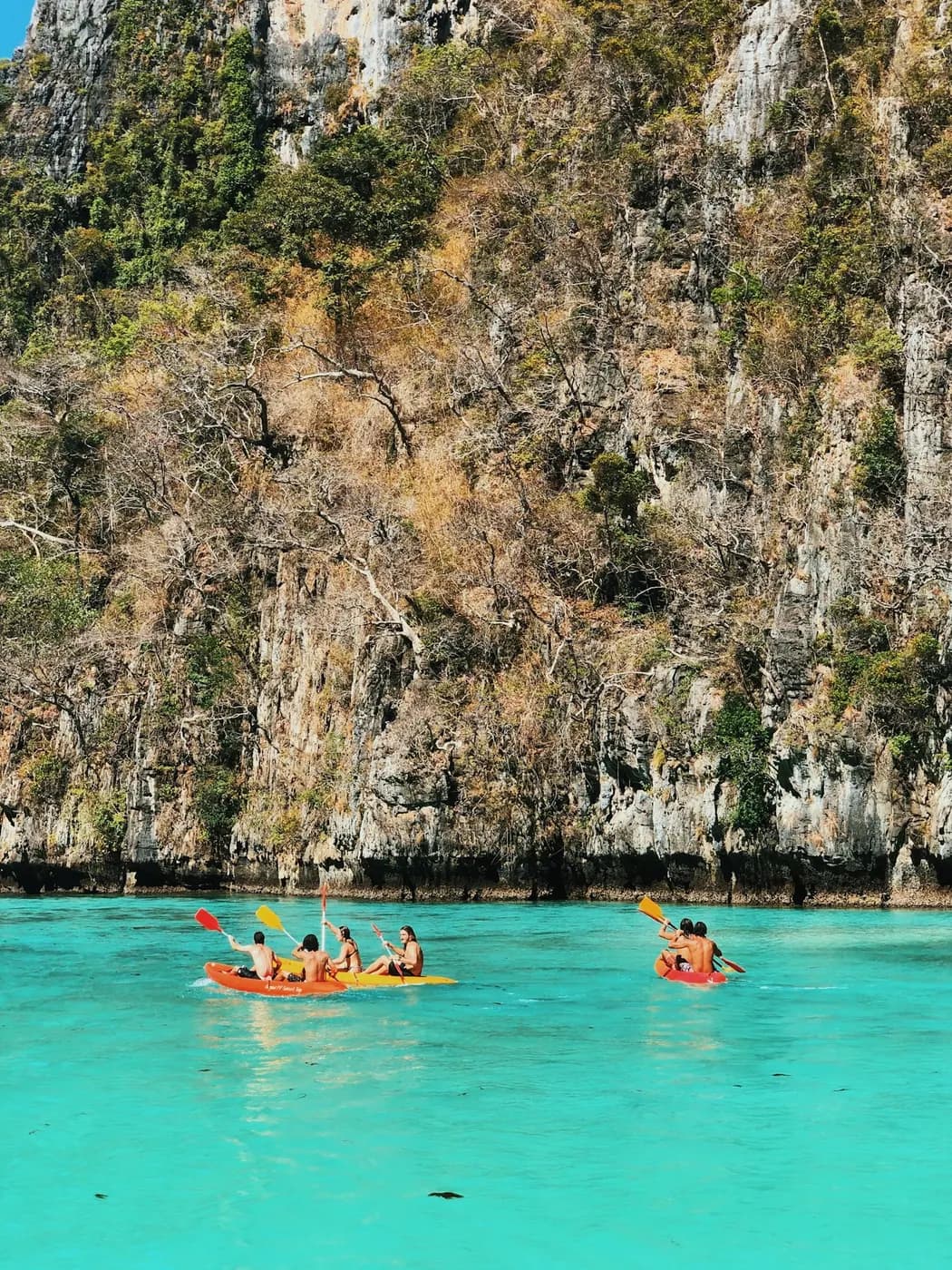 Kayakers paddling through turquoise water beneath tall cliffs